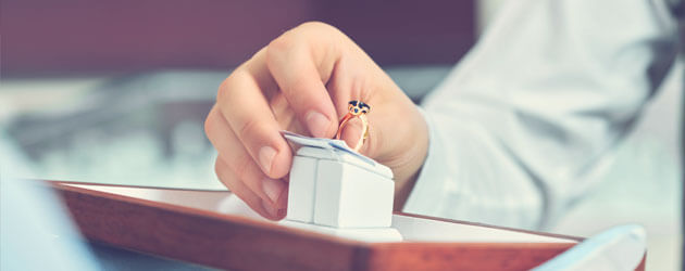 close up of hand grabbing gold band with dark stone ring from display box