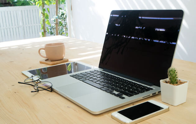 laptop on office desk next to phone and tablet