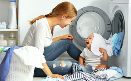 mom and baby playing with clothes in laundry room