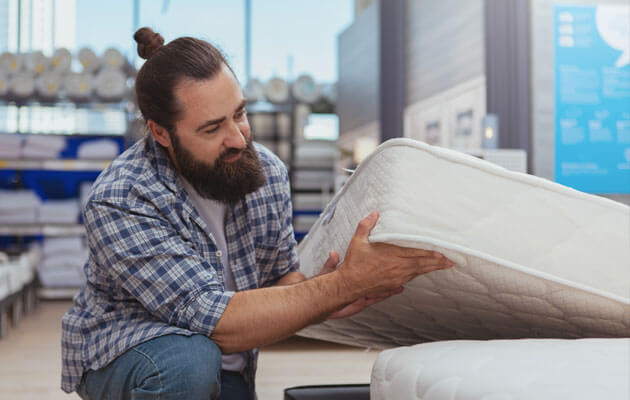 man holding up corner of mattress and evaluating