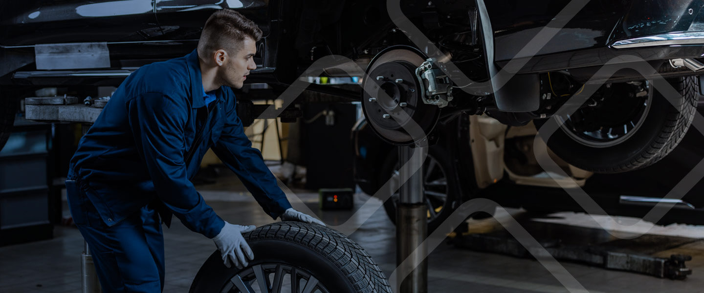 mechanic rolling tire to lifted car in shop