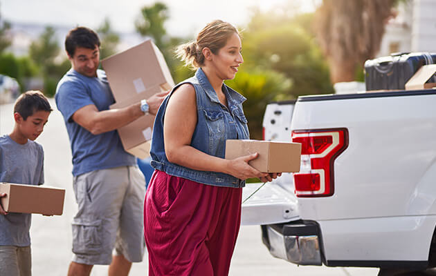 Hispanic family moving boxes out of pickup truck into house.