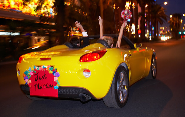 Newlyweds driving away in their new car.