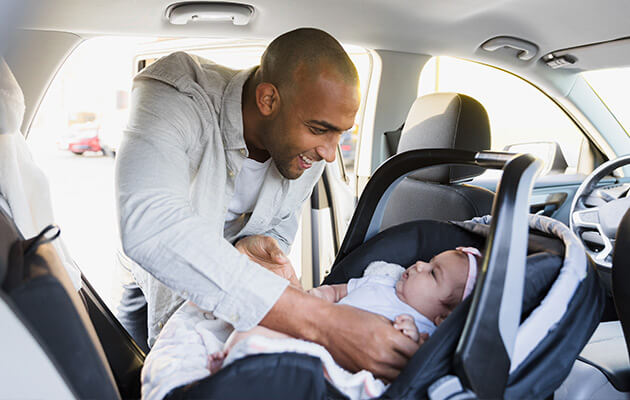 Smiling father puts baby in car seat.