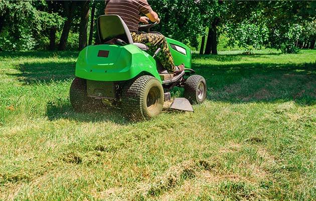 men riding green lawnmower cutting grass